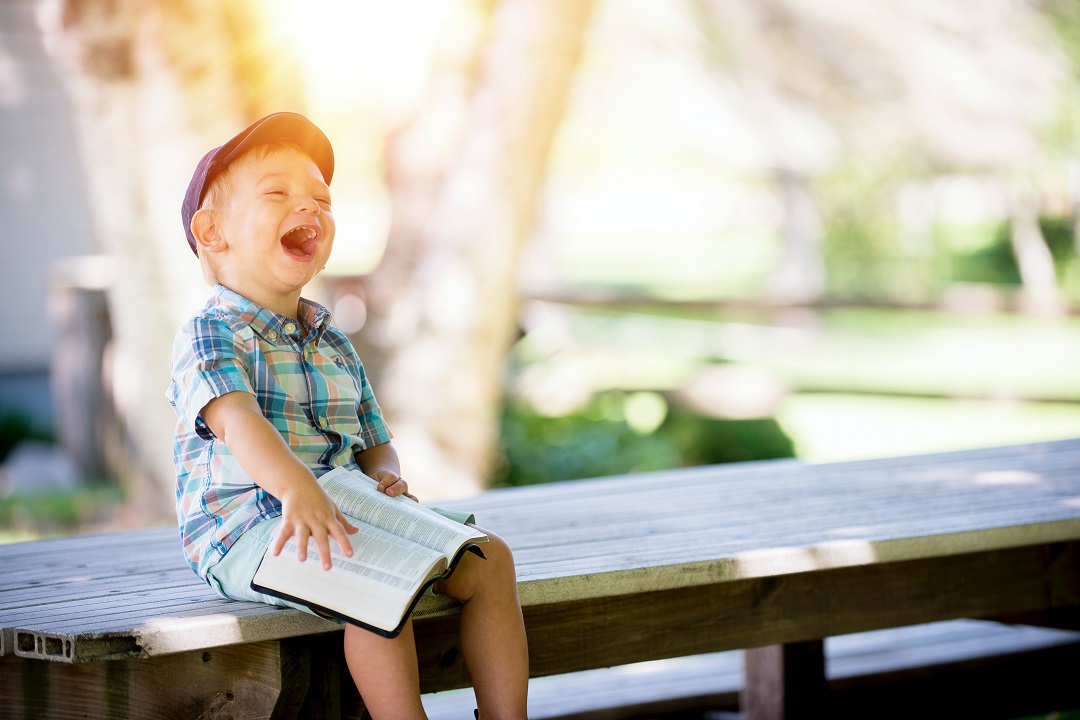 enfant assis sur un banc qui rit en lisant un livre