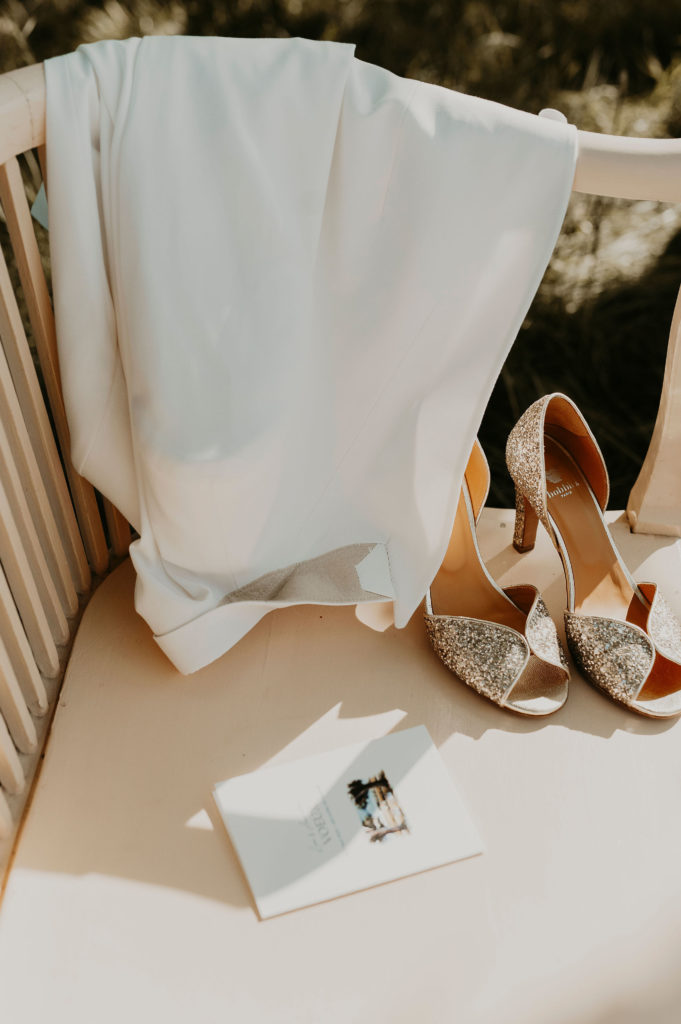 robe, chaussures de mariée et livret de cérénomie posé sur un banc